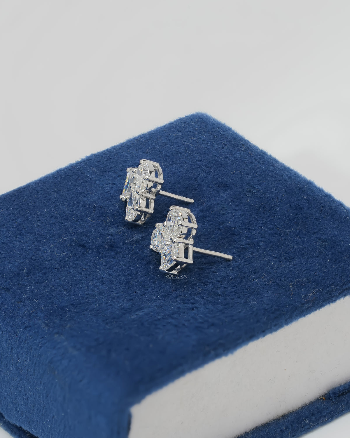 Side view of lab grown diamond cluster stud earrings in white gold with posts, resting on blue velvet