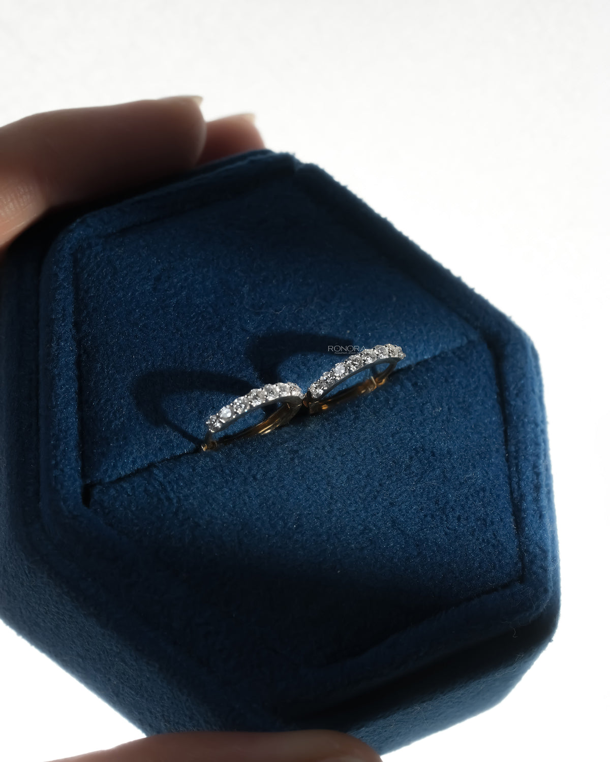 Pair of lab grown diamond huggie hoop earrings in a navy velvet jewelry box held in hand, backlit