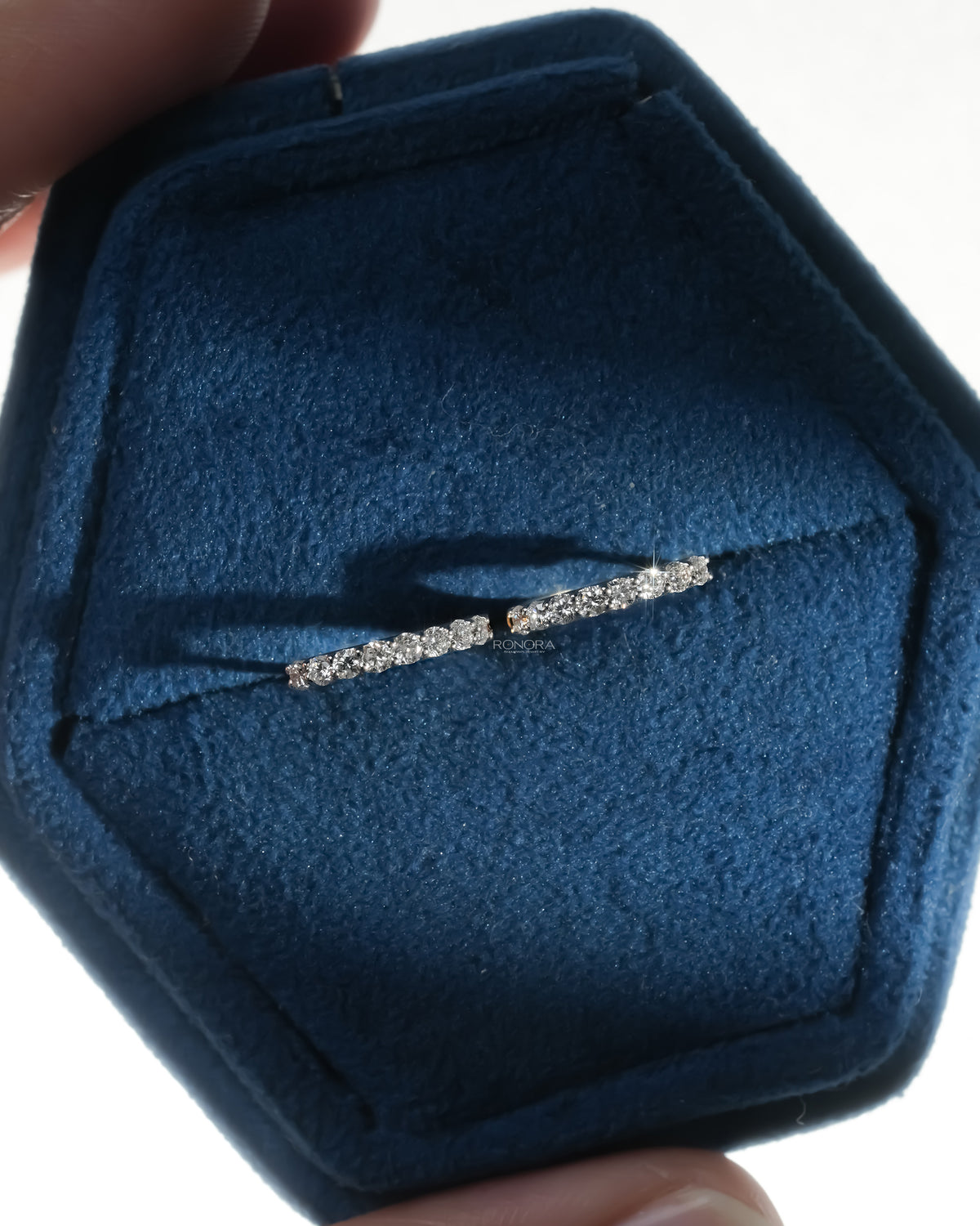 Pair of lab grown diamond huggie hoop earrings resting in a navy velvet hexagon jewelry box