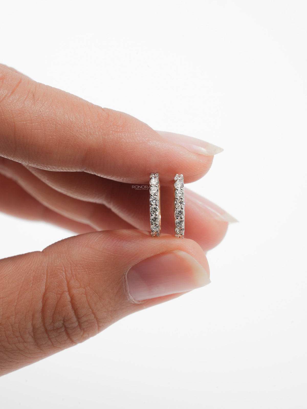 Pair of lab grown diamond huggie hoop earrings held between fingertips to show their small size