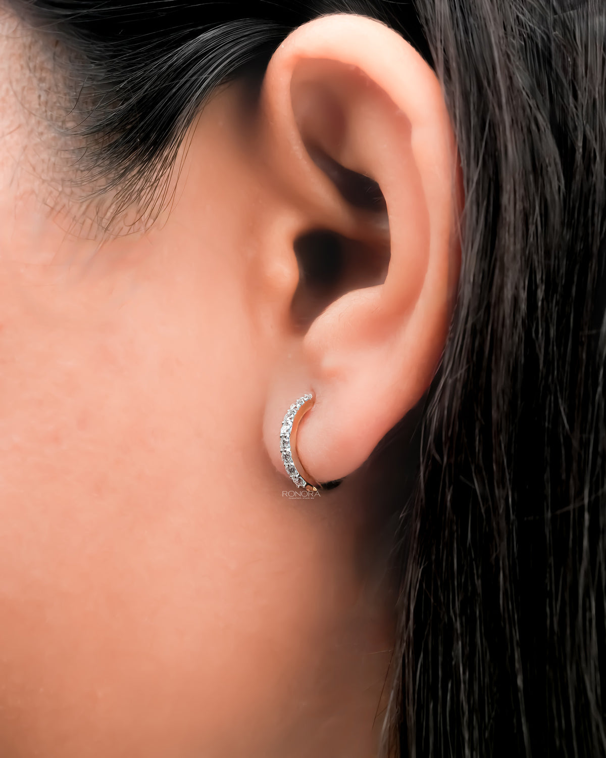 Close-up of a lab grown diamond huggie hoop earring worn on the ear, a single row of round diamonds