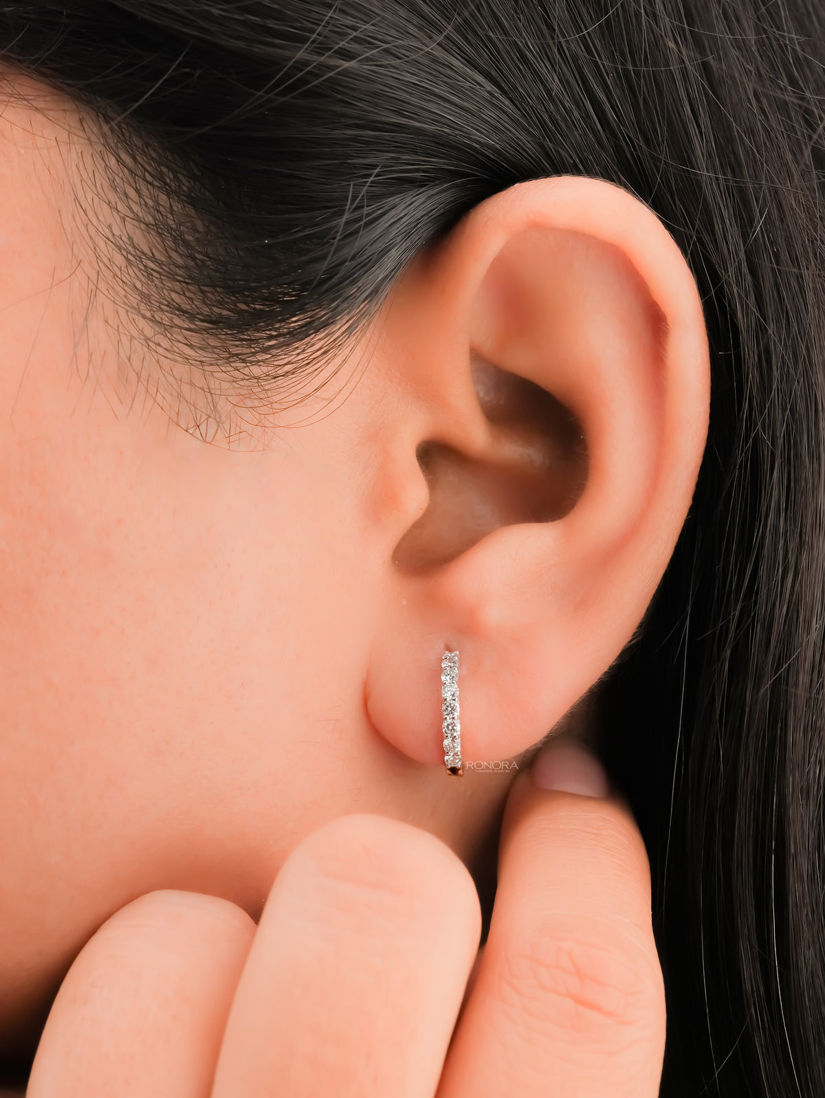 Lab grown diamond huggie hoop earring worn on the ear while a hand touches the jaw, row of round diamonds