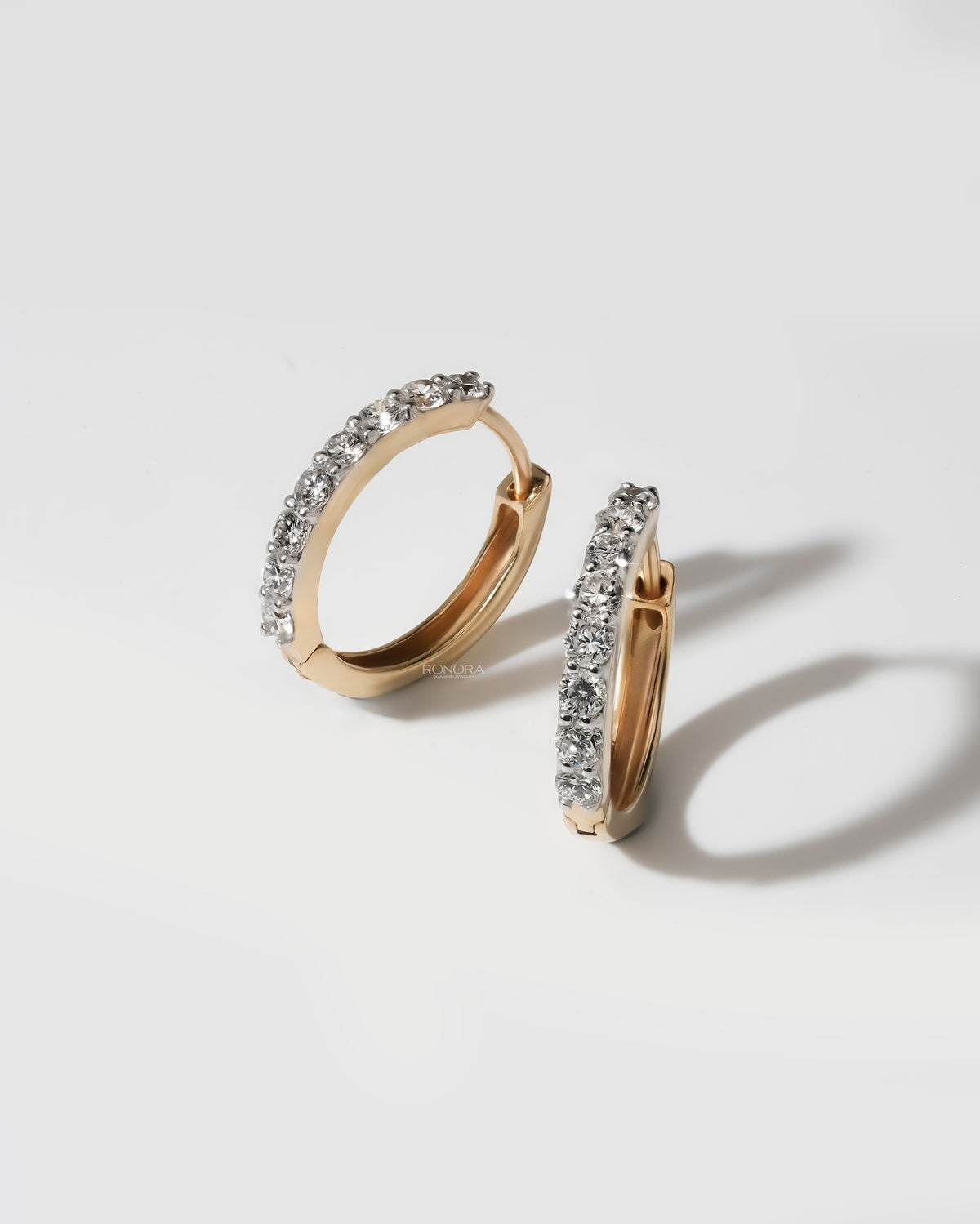 Pair of yellow gold lab grown diamond huggie hoop earrings on a white surface, one standing and one angled