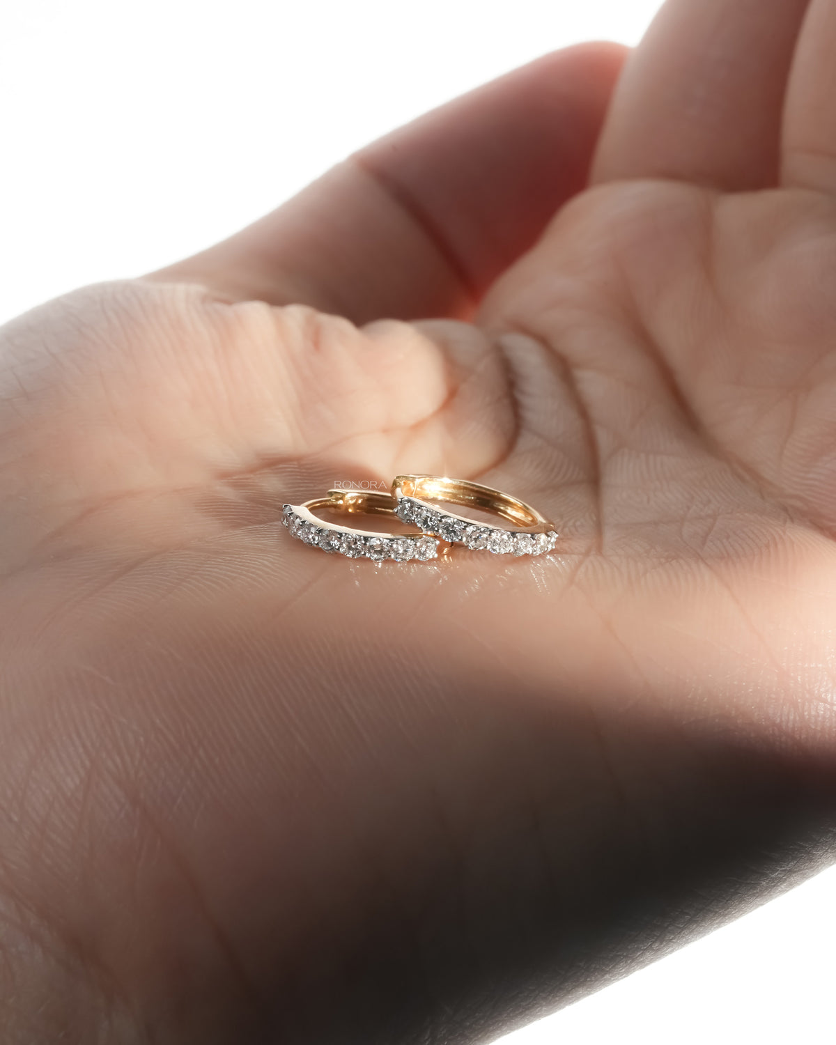 Pair of yellow gold lab grown diamond huggie hoop earrings resting on an open palm in warm light
