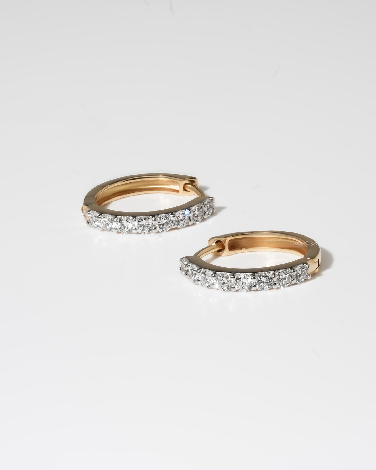 Side view of two yellow gold lab grown diamond huggie hoop earrings lying flat, showing the row of round diamonds