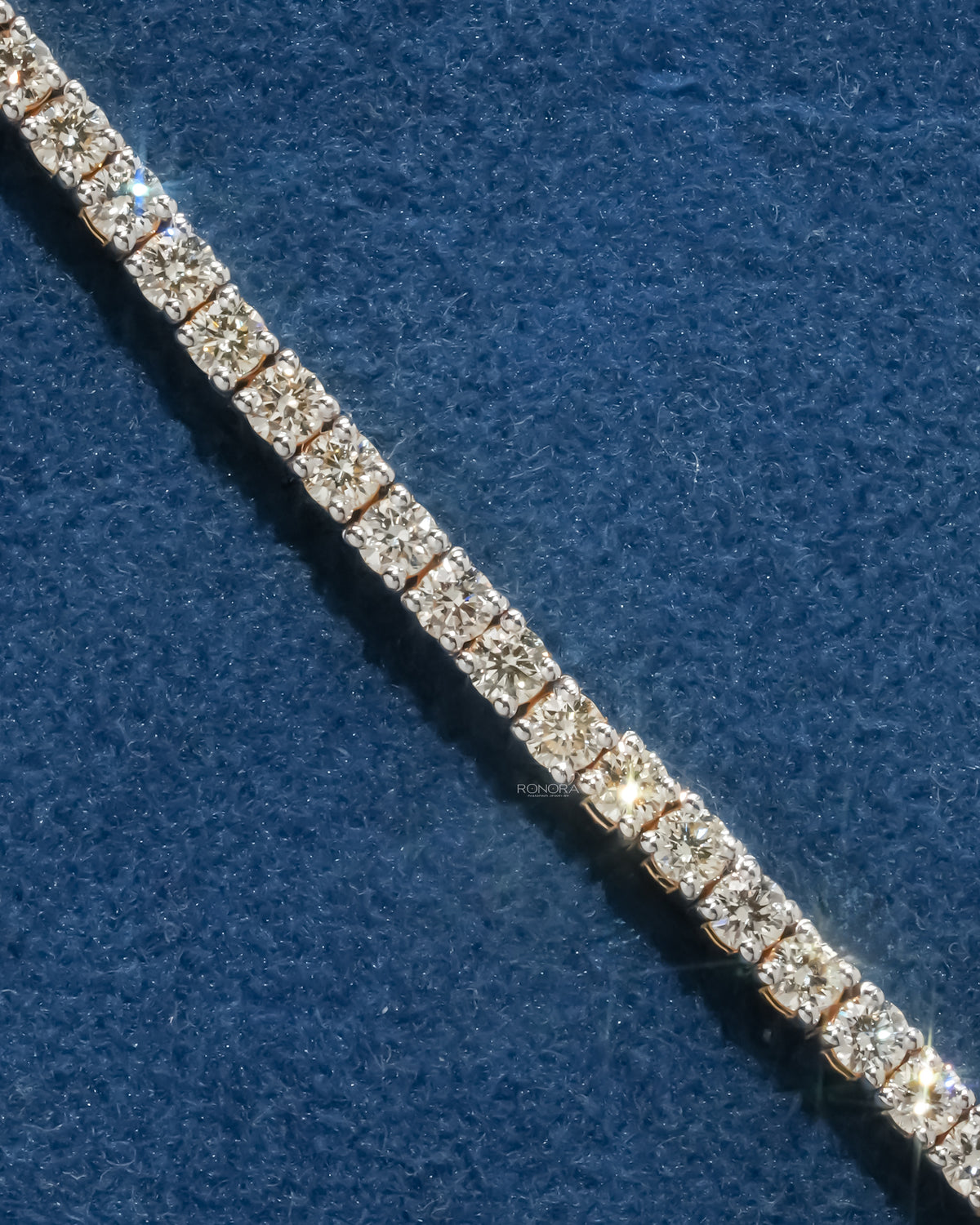 Close-up of round lab grown diamond tennis bracelet stones sparkling on a blue velvet surface