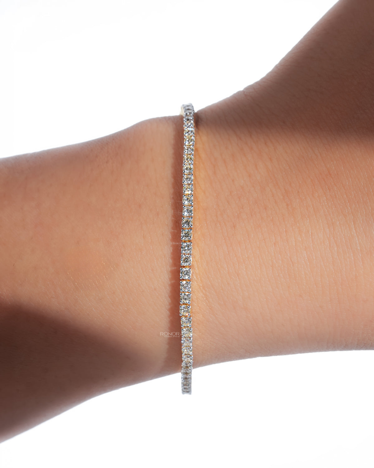 Dainty lab grown diamond tennis bracelet worn on a wrist, a slim line of round white diamonds in soft sunlight