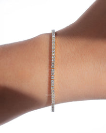 Dainty lab grown diamond tennis bracelet worn on a wrist, a slim line of round white diamonds in soft sunlight