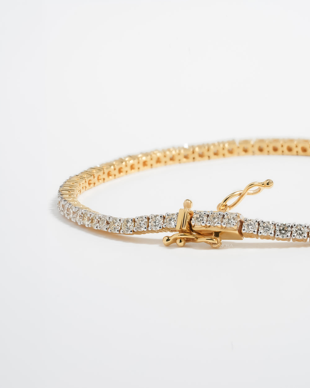 Angled view of a yellow gold lab grown diamond tennis bracelet showing the box clasp, safety latch and round stones