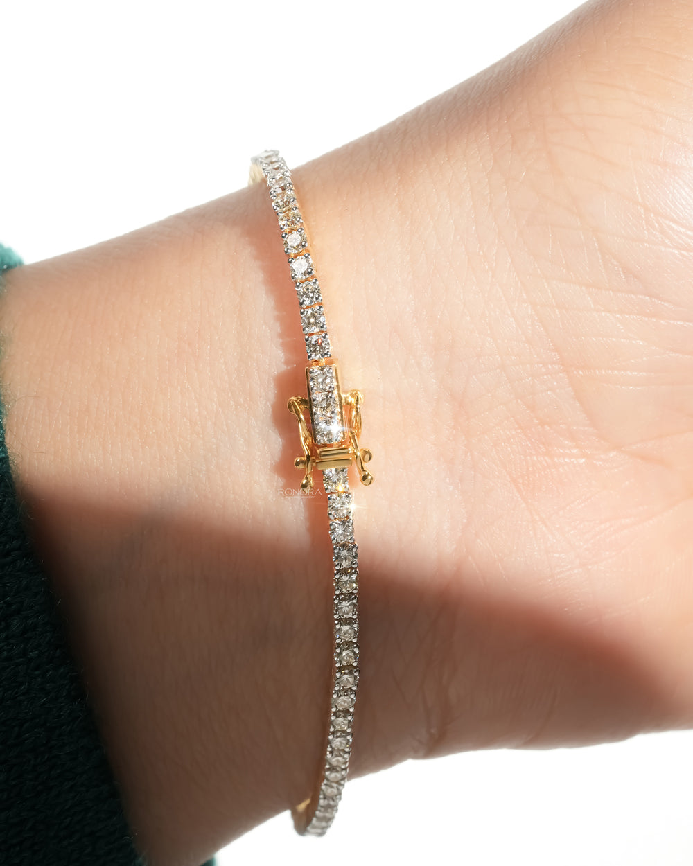 Lab grown diamond tennis bracelet on a wrist with its yellow gold box clasp and a line of round diamonds