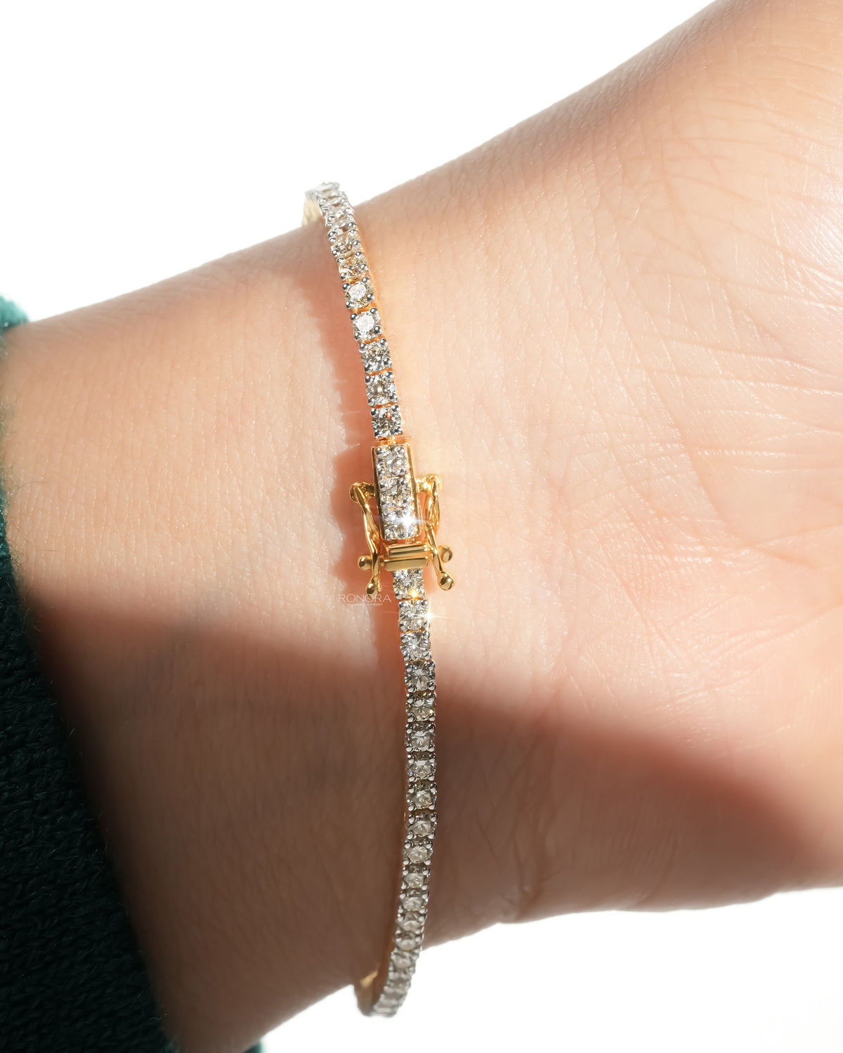 Lab grown diamond tennis bracelet on a wrist with its yellow gold box clasp and a line of round diamonds