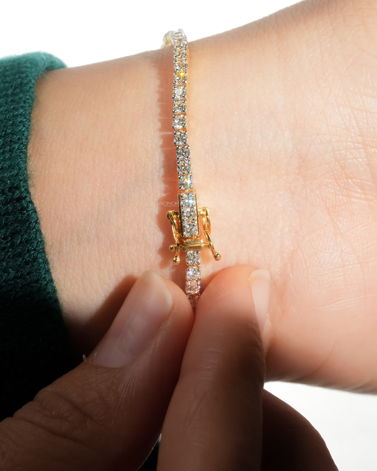 Fingers closing the yellow gold box clasp of a round lab grown diamond tennis bracelet on a wrist