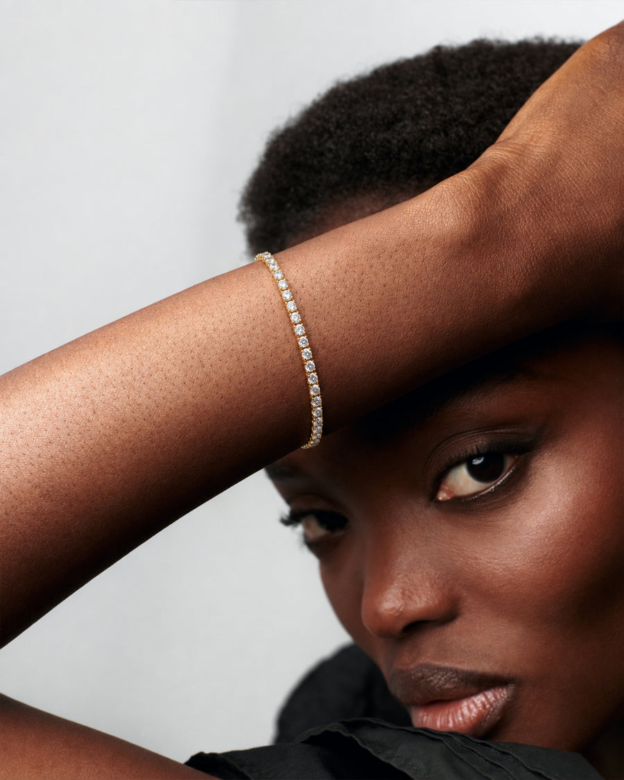 Model resting her arm on her head wearing a dainty yellow gold lab grown diamond tennis bracelet with round stones