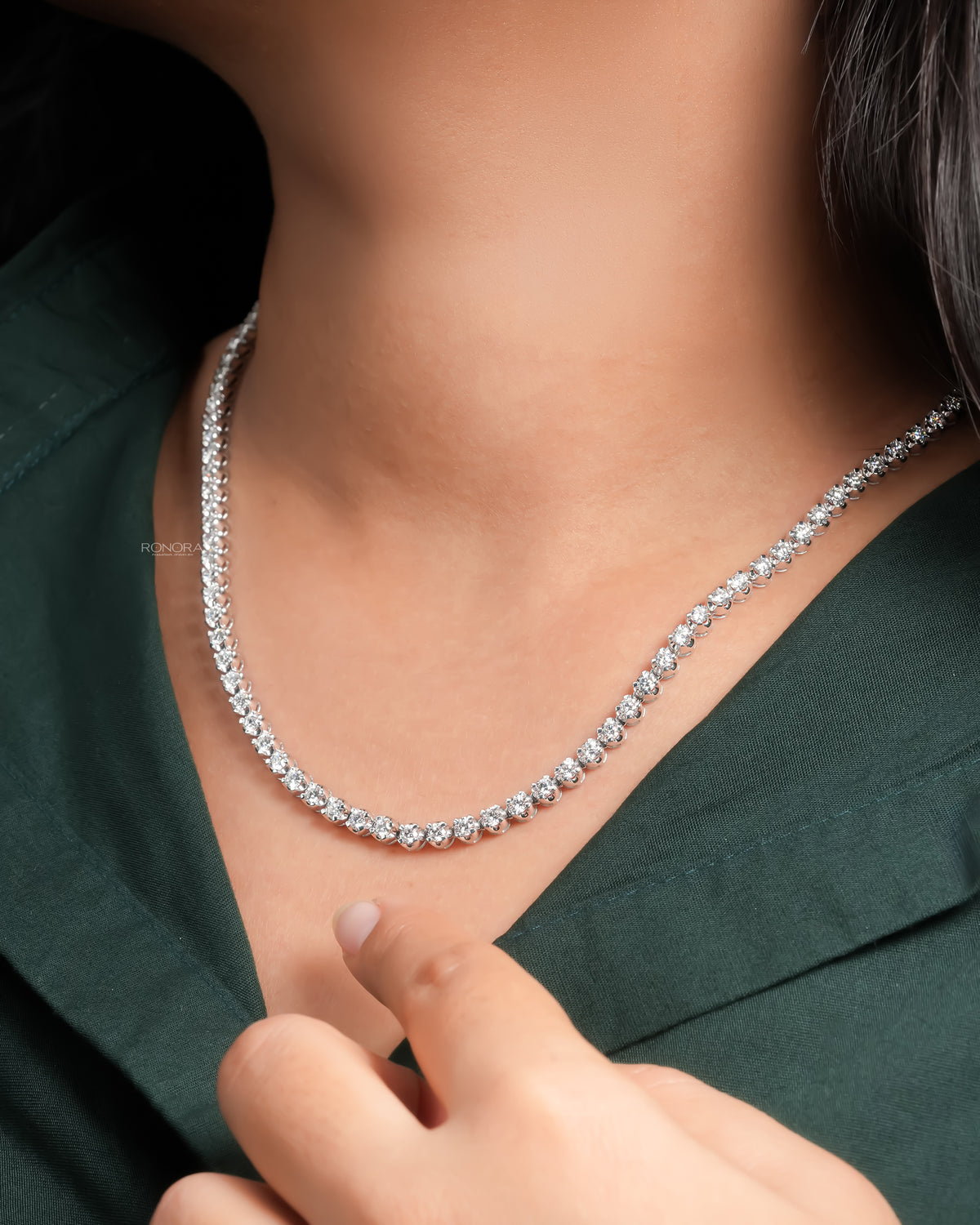 Lab grown diamond tennis necklace worn by a woman, her hand resting near a green shirt collar