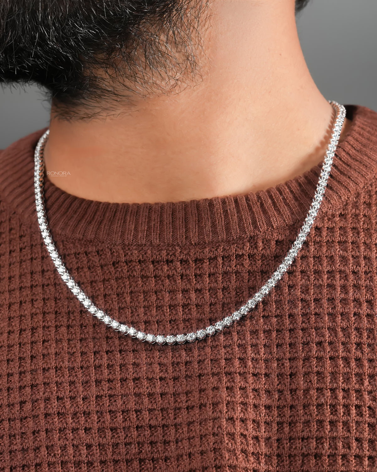 Man wearing a round lab grown diamond tennis necklace over a rust brown waffle knit sweater