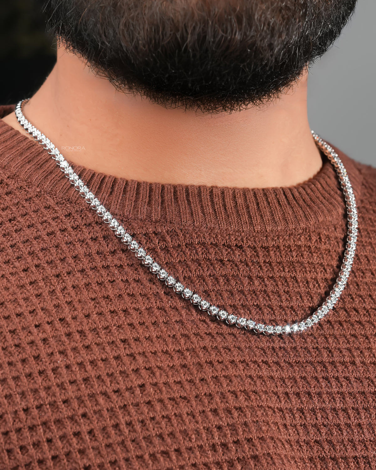 Round lab grown diamond tennis necklace on a man's neck, curving over a brown knit sweater