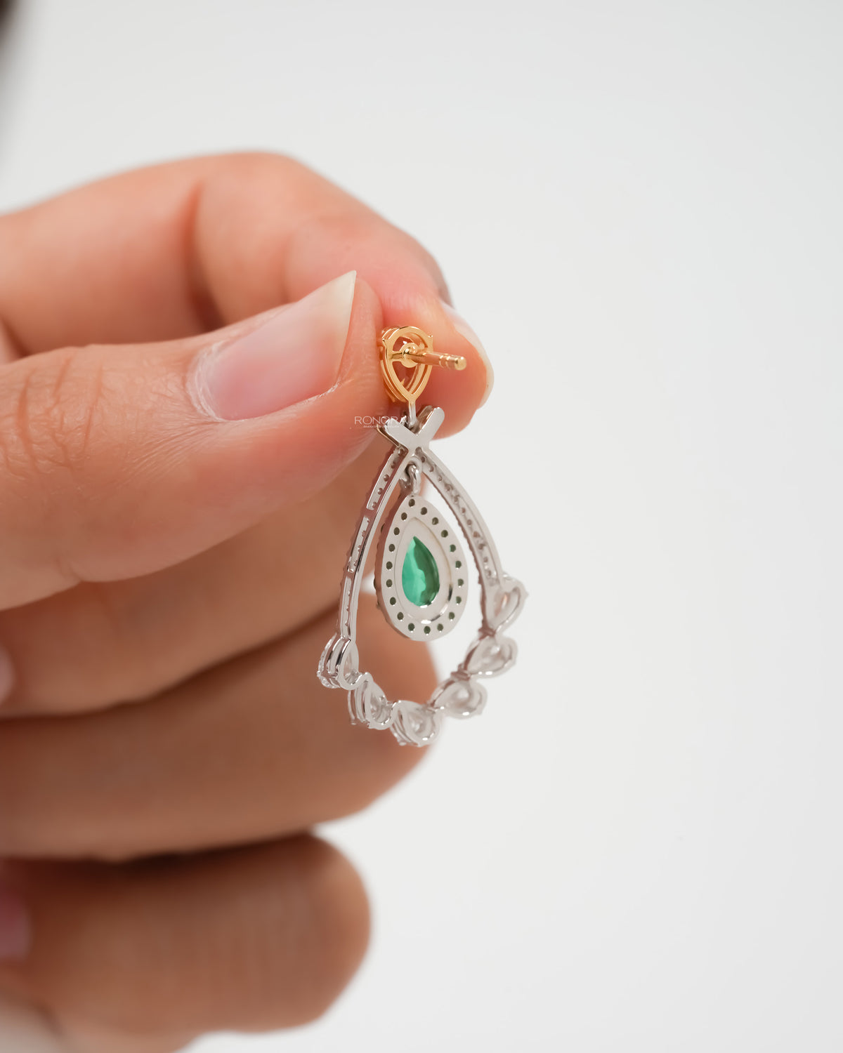 Back of lab grown emerald pear drop earrings held in fingers, showing the yellow gold post and diamond frame