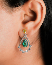 Close-up of an ear wearing a lab grown emerald pear drop earring with green halo and a yellow pear top