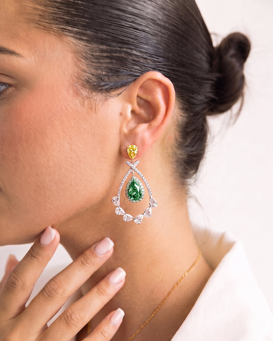 Woman wearing lab grown emerald pear drop earrings with a yellow pear top and white diamond teardrop frame