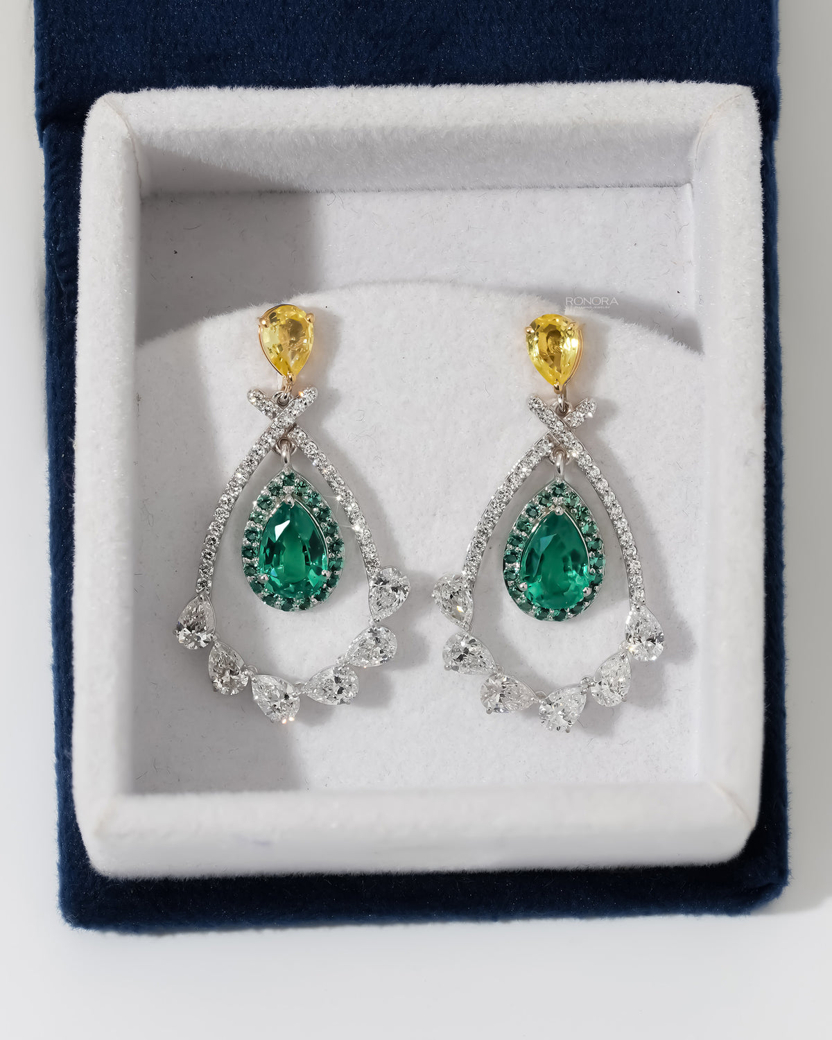 Top view of lab grown emerald pear drop earrings with yellow pear tops in a white velvet jewelry box