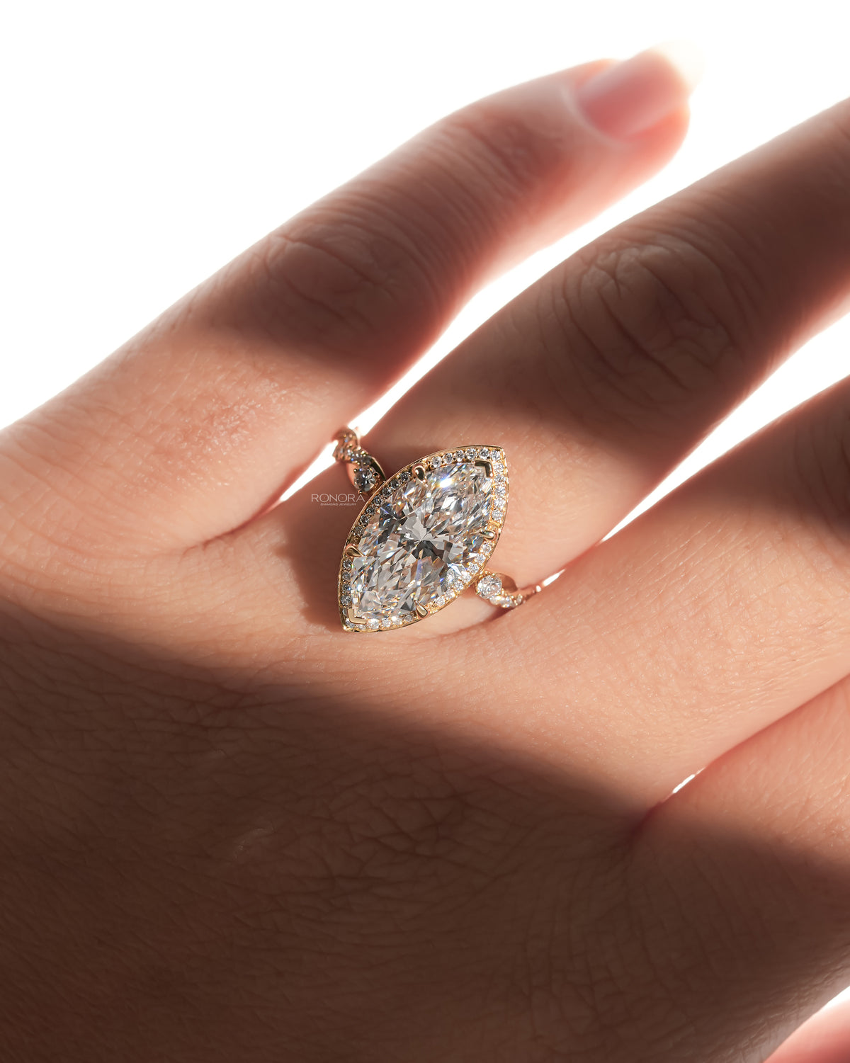 Hand wearing a marquise halo lab grown diamond ring with a pave halo and twisted gold band in soft sunlight
