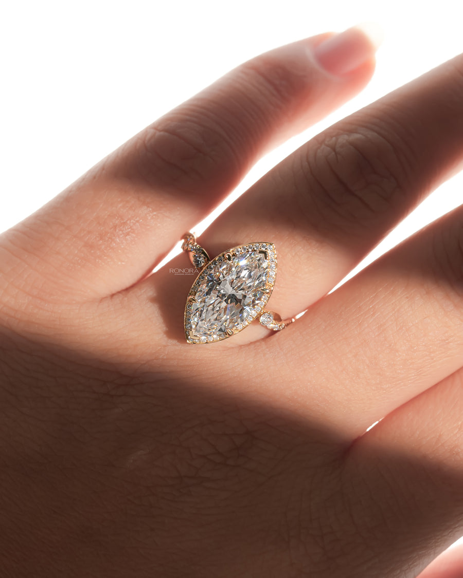 Hand wearing a marquise halo lab grown diamond ring with a pave halo and twisted gold band in soft sunlight
