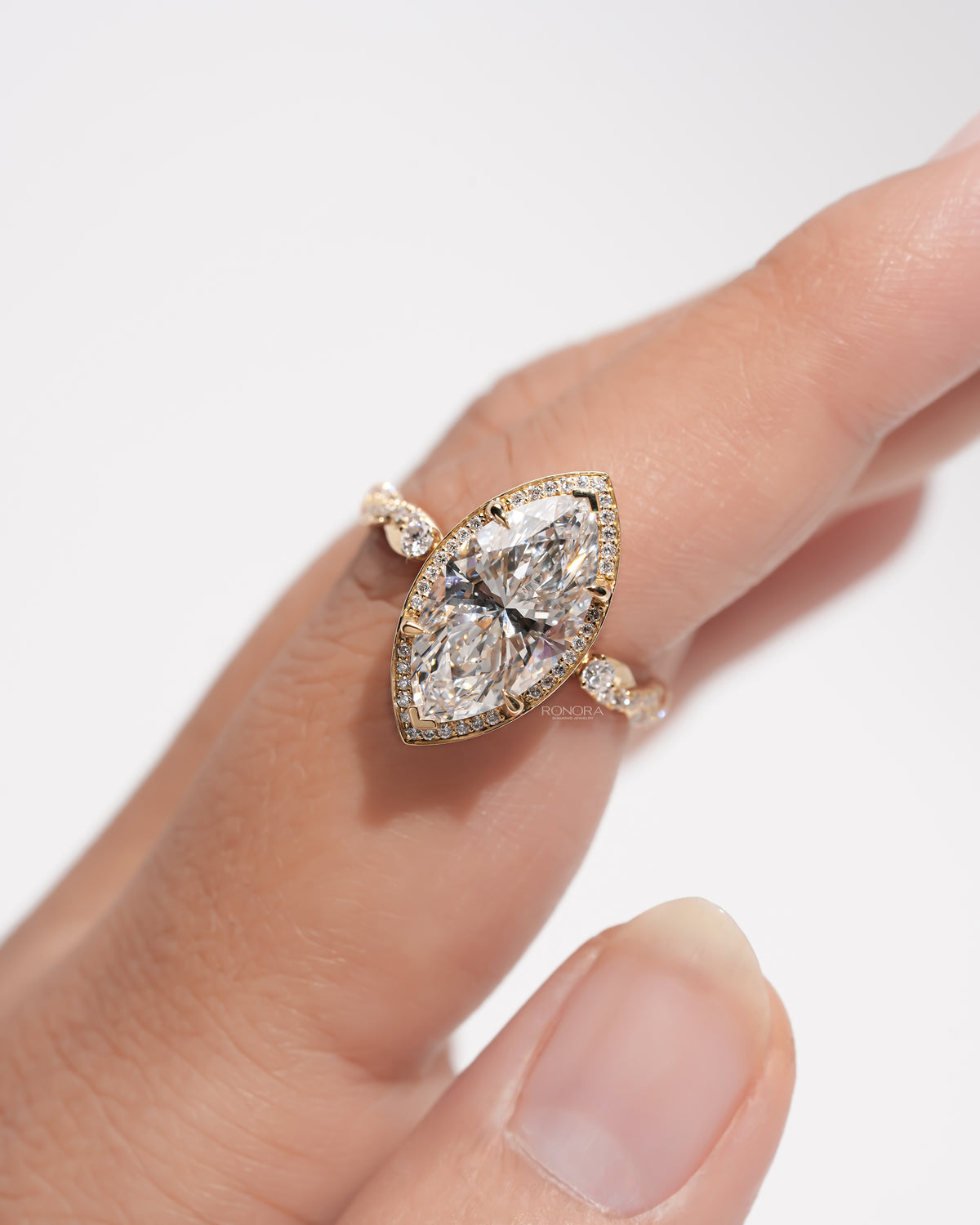 Hand wearing a marquise halo lab grown diamond ring in yellow gold, angled view of the twisted pave band