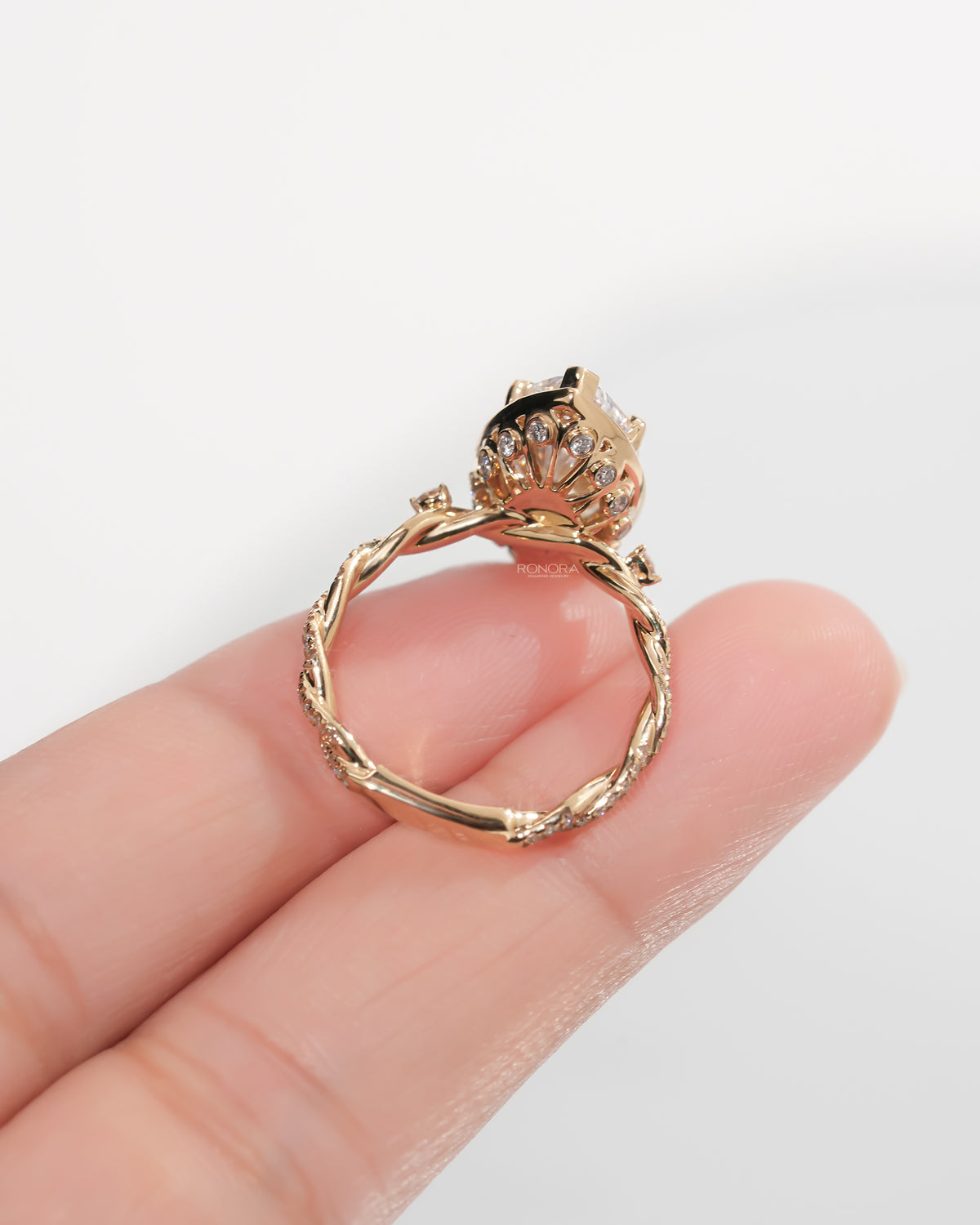 Back view of a yellow gold marquise halo lab grown diamond ring held on a hand, showing the twisted band and gallery