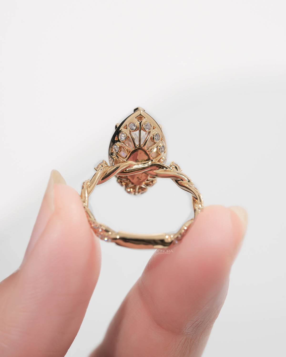 Back view of a marquise halo lab grown diamond ring in yellow gold held between fingers, showing its open gallery