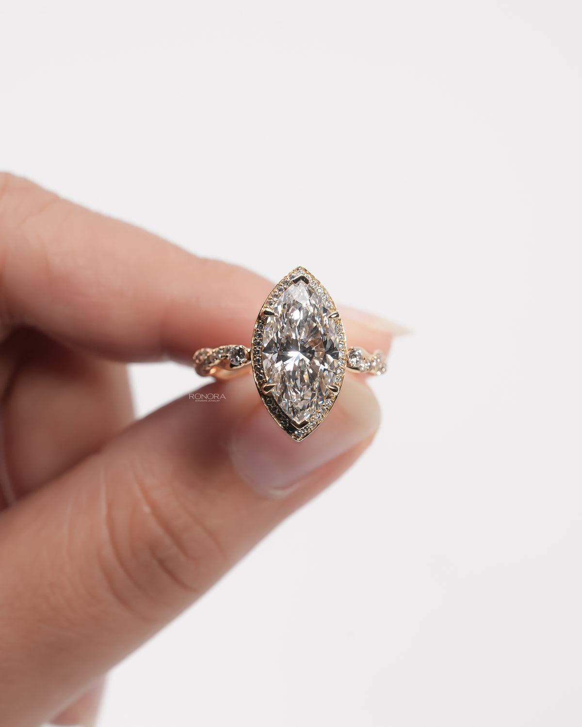 Front view of a marquise halo lab grown diamond ring in yellow gold held between fingers, showing the pave halo