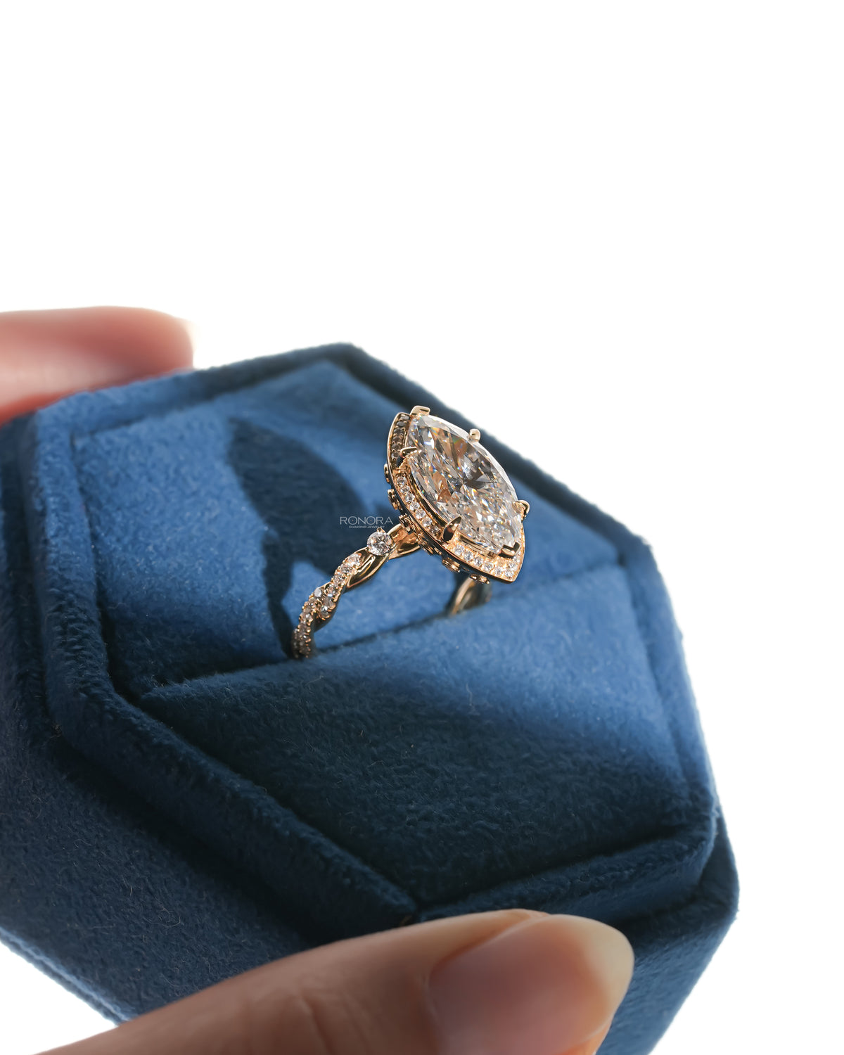 Angled view of a marquise halo lab grown diamond ring with a pave twist band in a blue velvet ring box