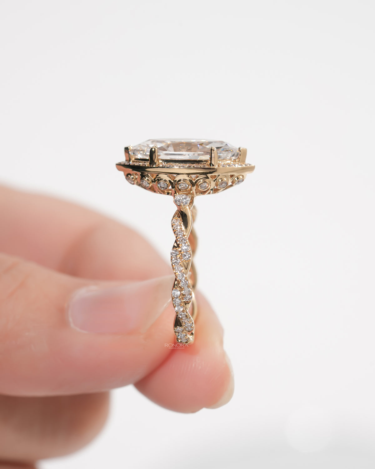 Side view of a marquise halo lab grown diamond ring in yellow gold held between fingers, pave twist band visible