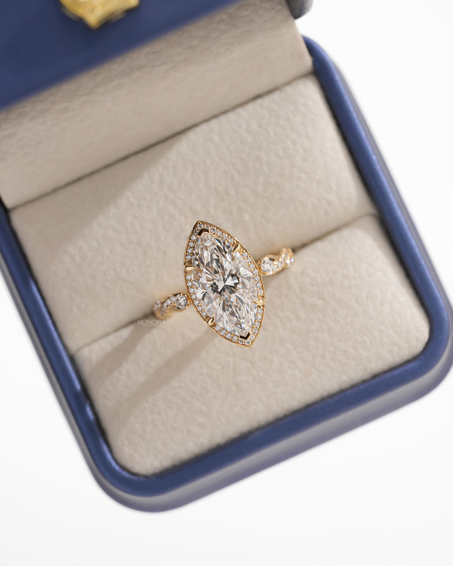 Top view of a marquise halo lab grown diamond ring in yellow gold set in a navy and cream jewelry box