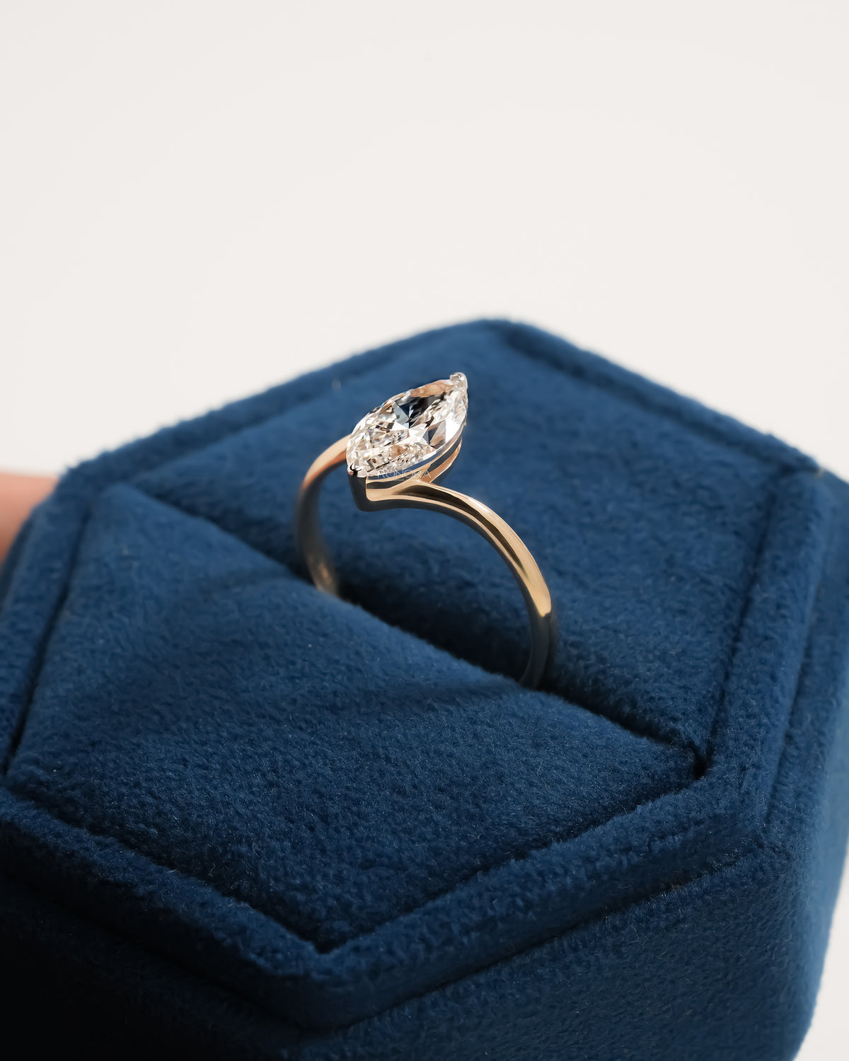 Marquise lab grown diamond bypass ring standing in a blue velvet jewelry box, gold band wrapping the stone