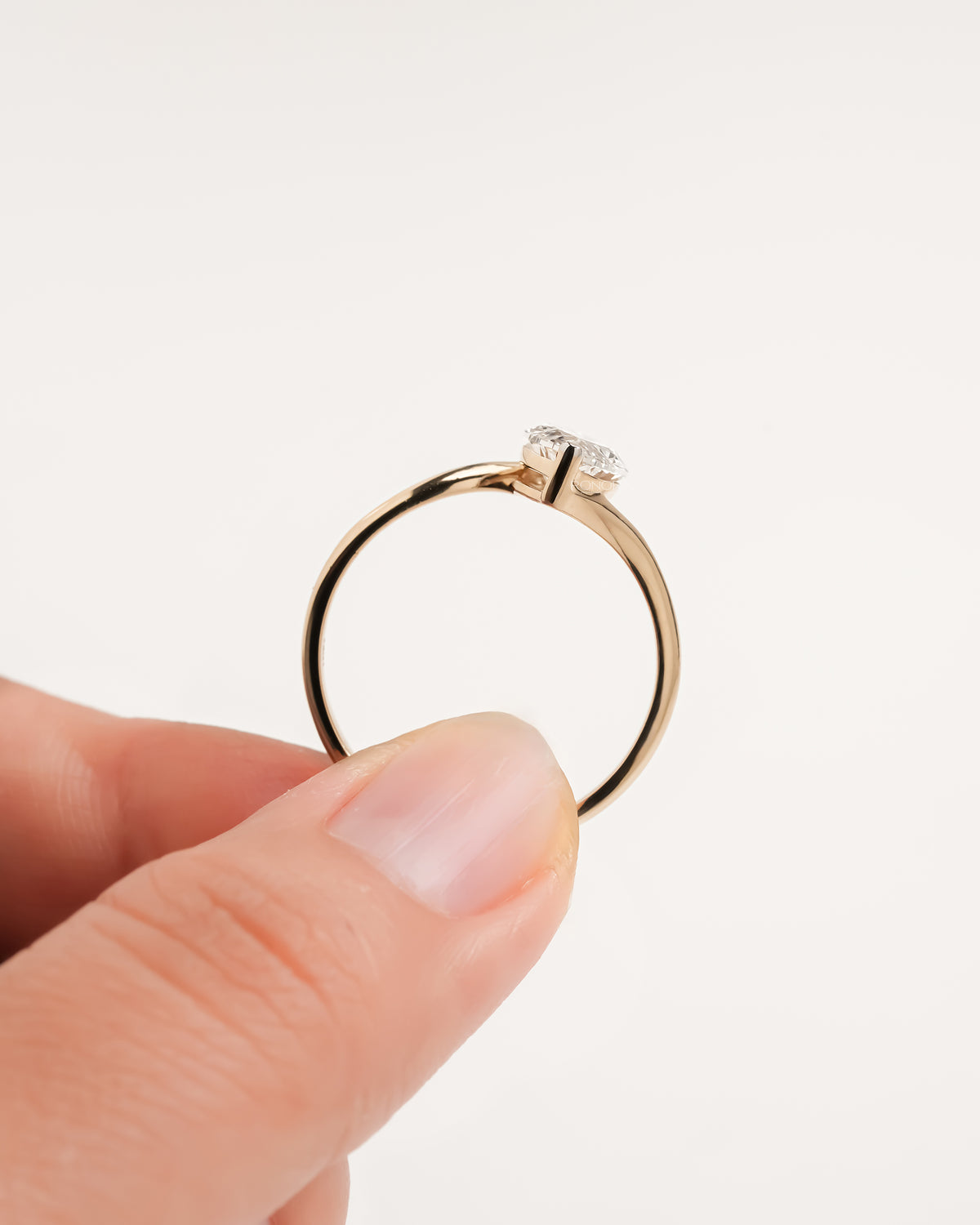 Marquise lab grown diamond bypass ring held upright between thumb and finger, showing the band profile