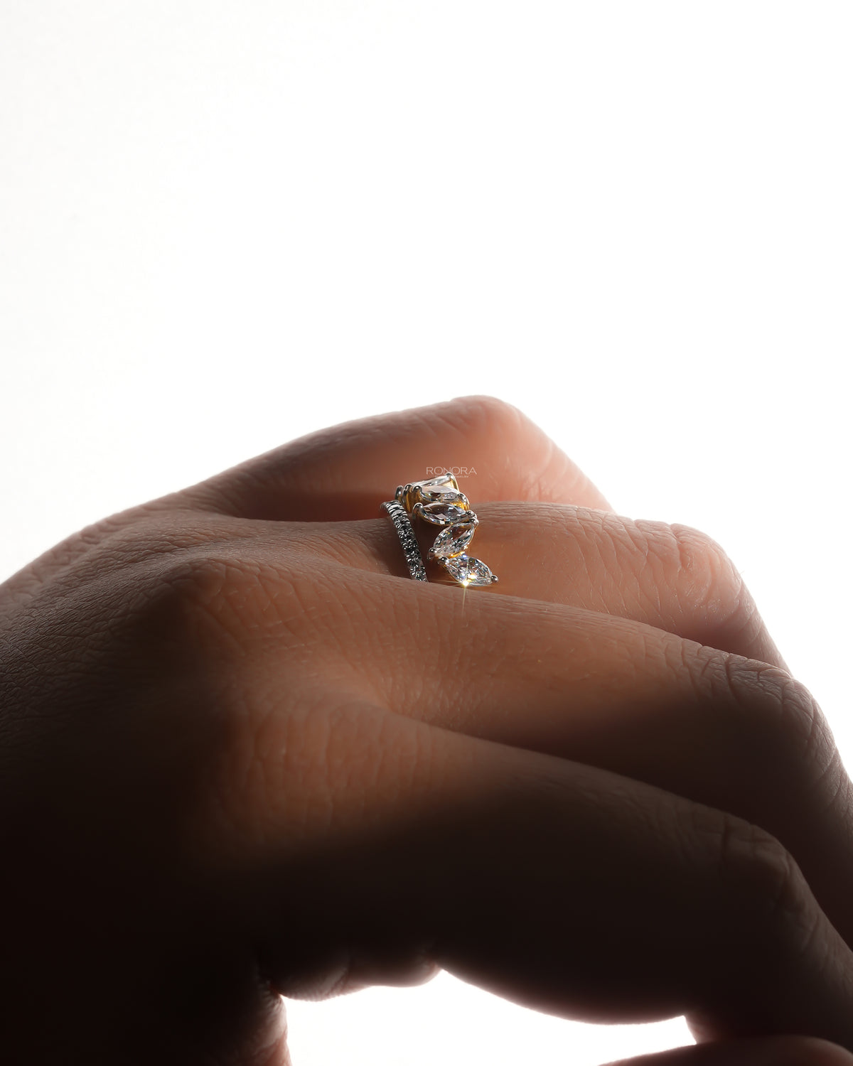 Side view of a marquise lab grown diamond leaf wrap ring worn on a backlit finger with a pave band beside the leaves