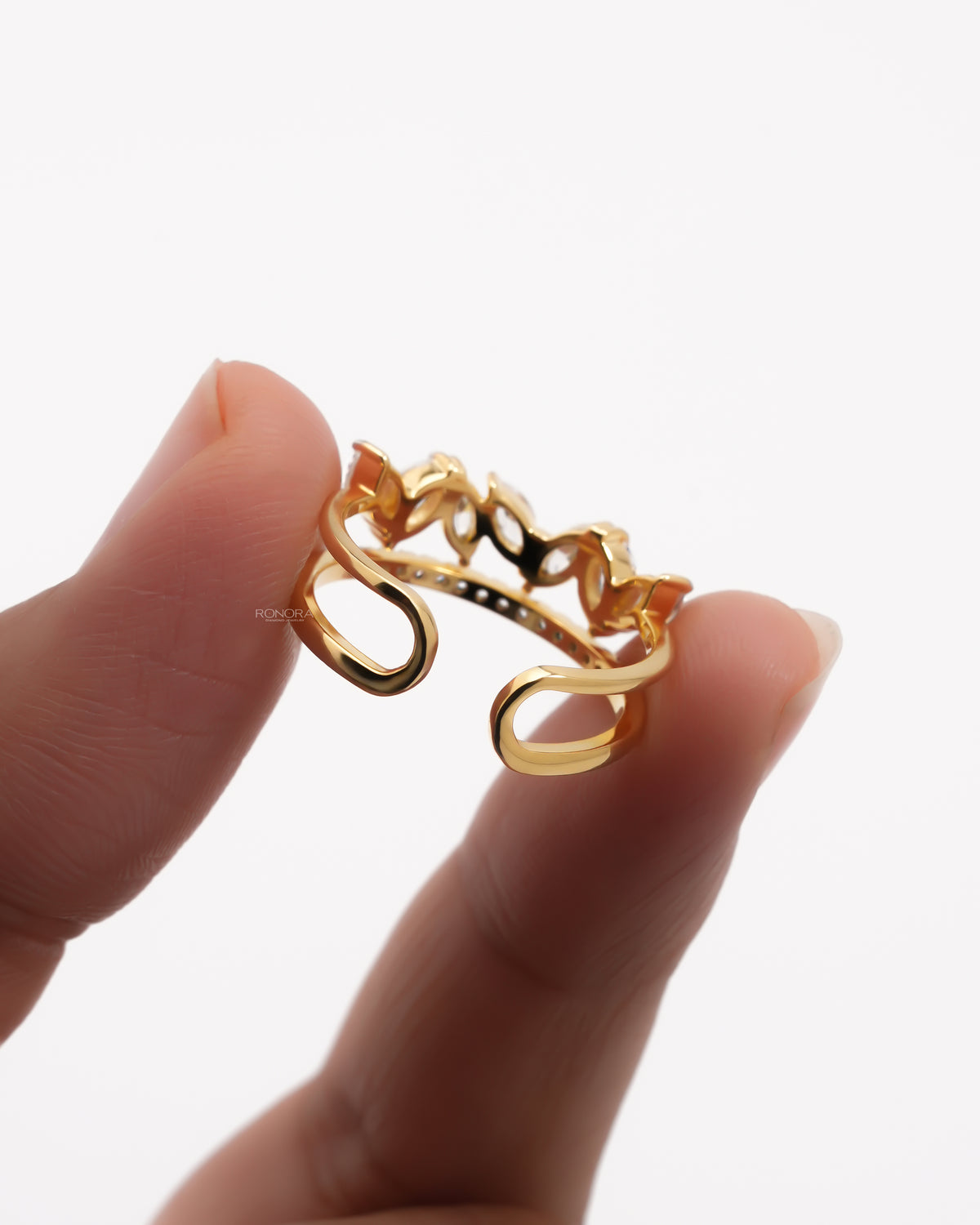 Back view of a yellow gold marquise lab grown diamond leaf wrap ring held between fingers showing the open wrap shank