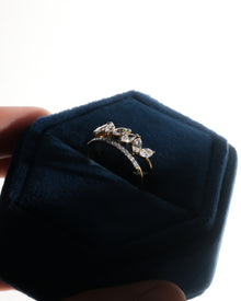 Marquise lab grown diamond leaf wrap ring in yellow gold standing in a dark blue velvet ring box with a pave band