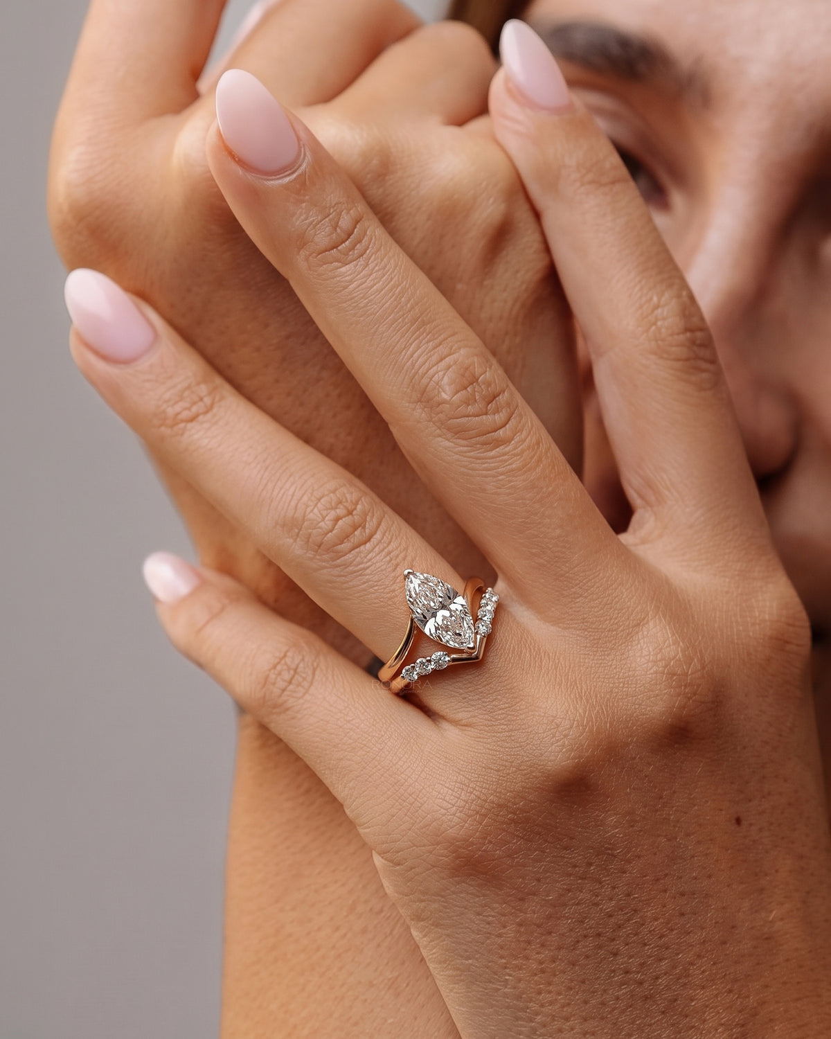Hands framing a face wearing a marquise lab grown diamond ring set with a rose gold V shaped diamond band