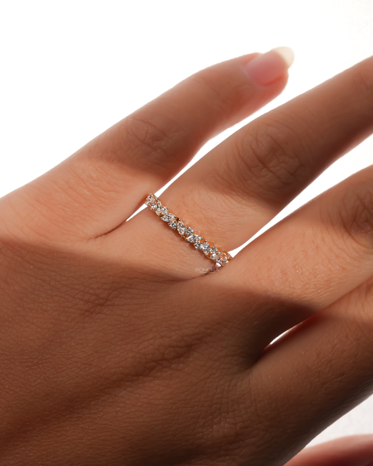 Hand wearing a marquise and round lab grown diamond wedding band, the stones set in a leaf vine pattern