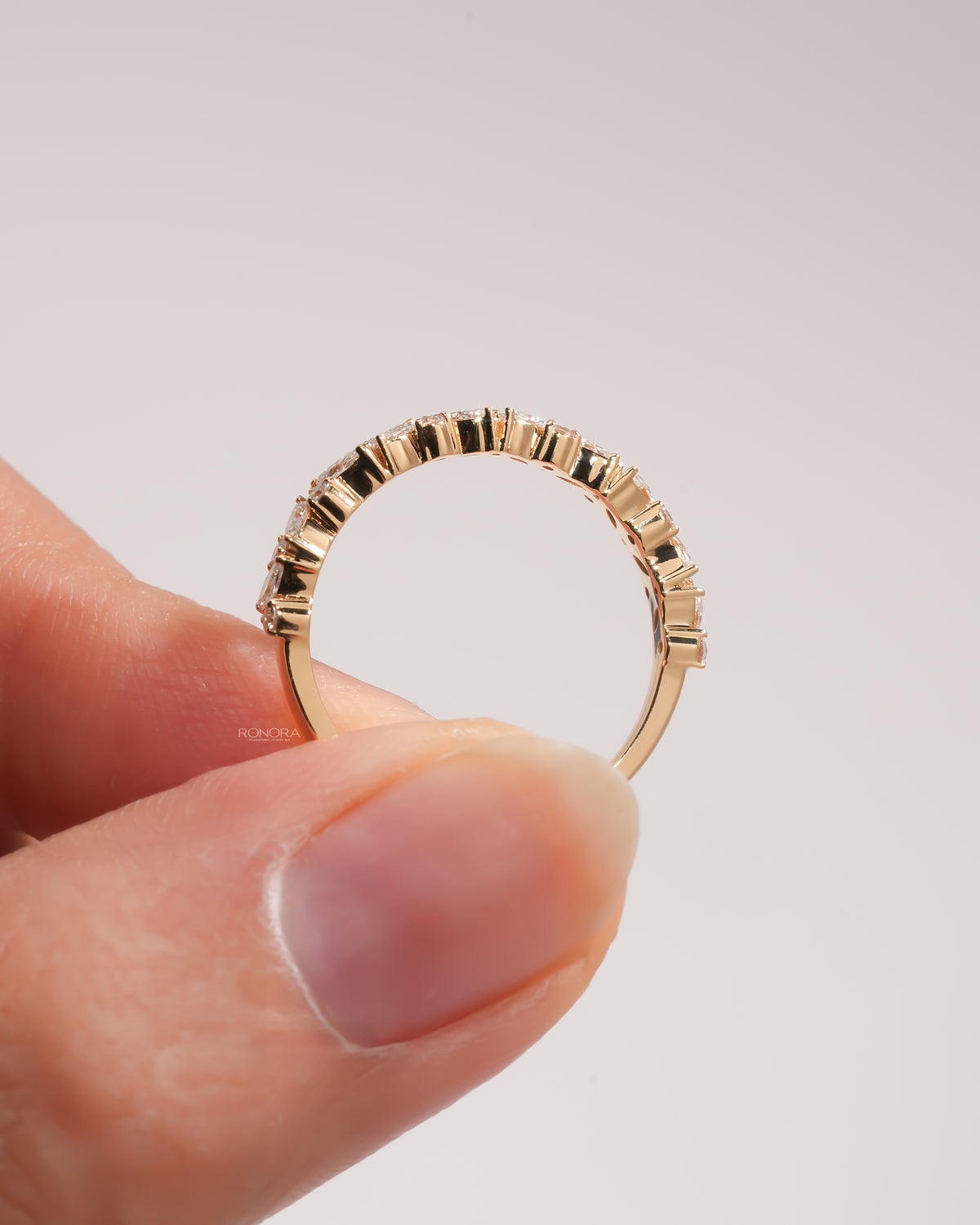 Yellow gold marquise and round lab grown diamond wedding band held between two fingers, side profile of the setting