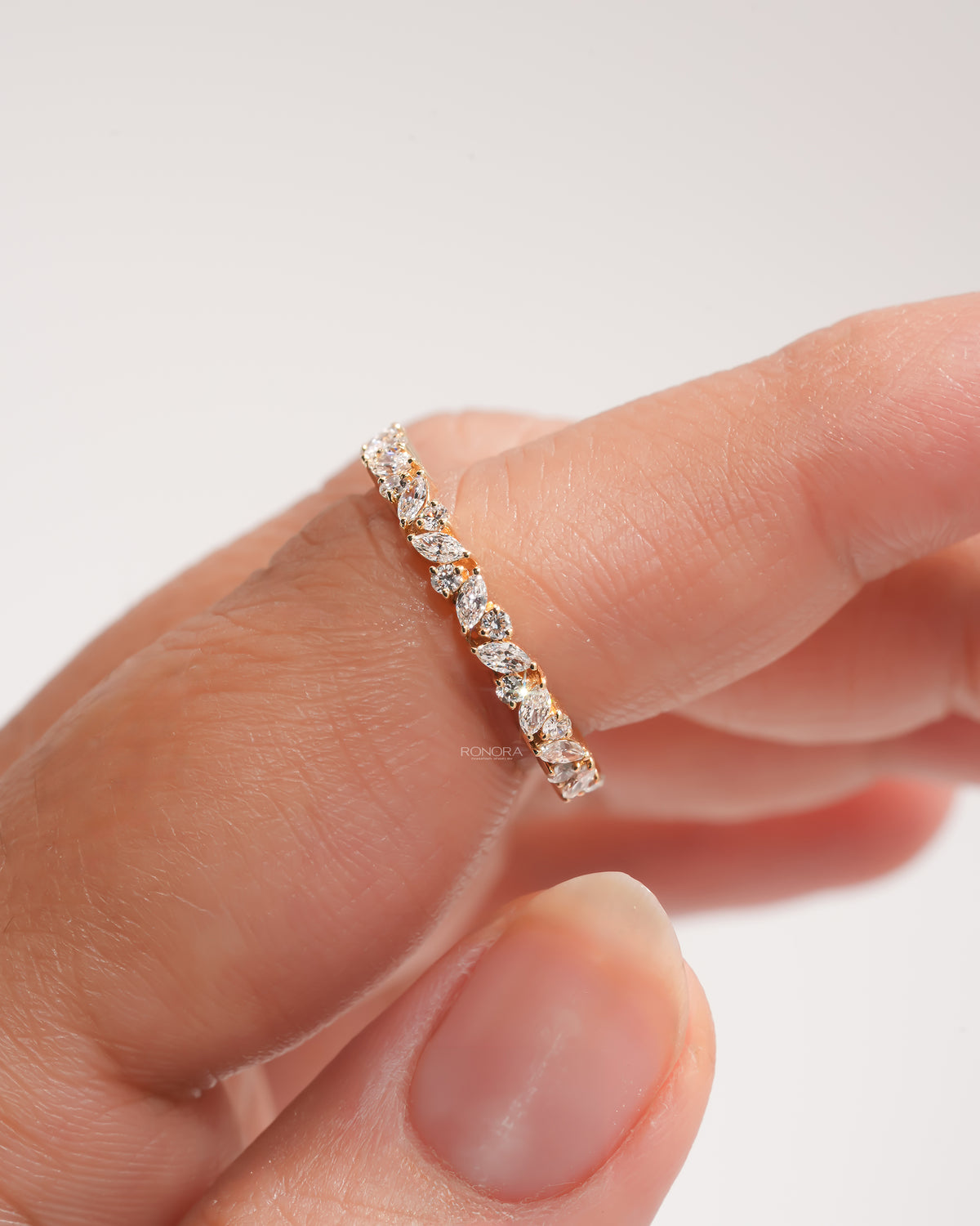 Close-up of a marquise and round lab grown diamond wedding band in yellow gold on a fingertip, leaf vine design