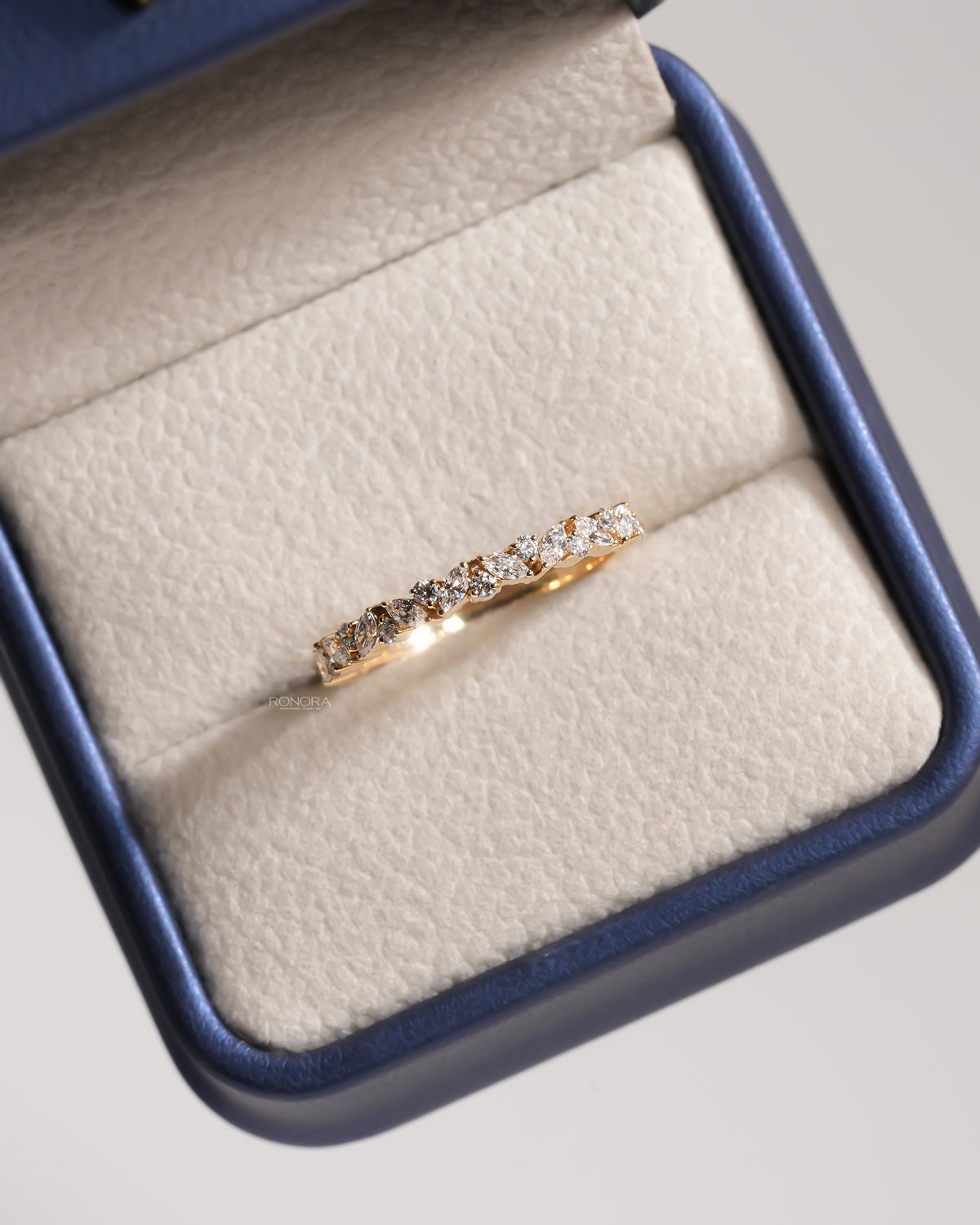 Marquise and round lab grown diamond wedding band in yellow gold resting in a blue ring box, top view