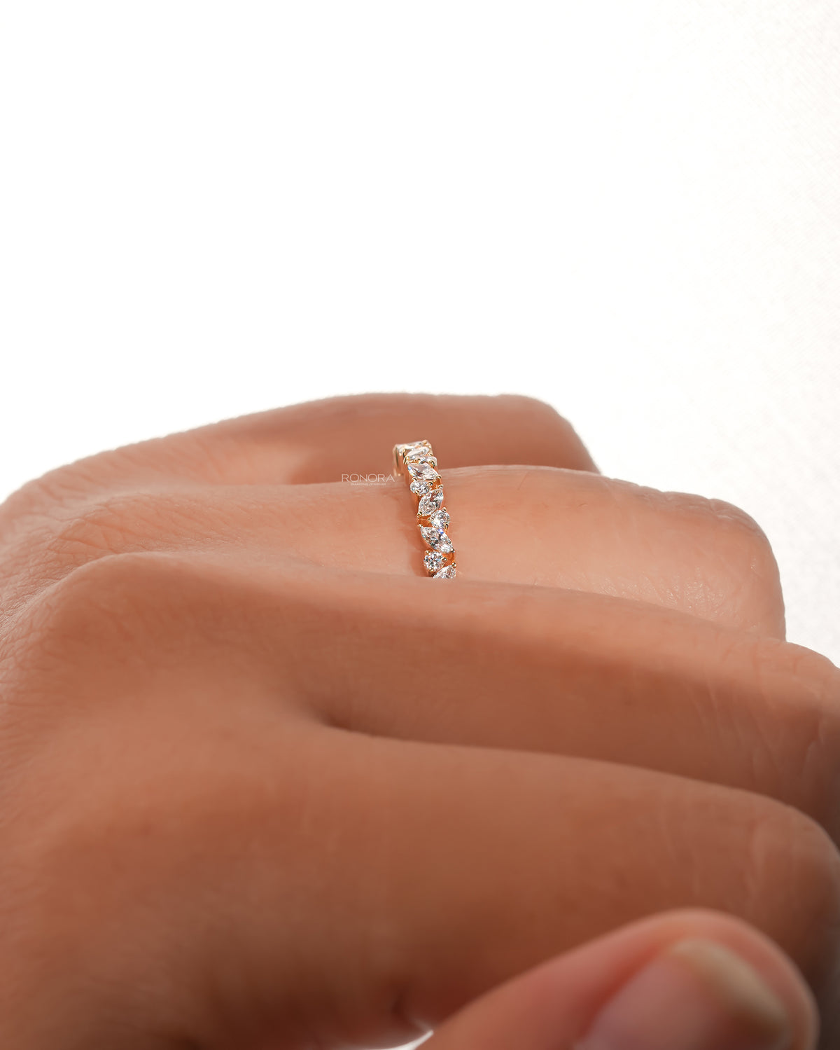 Side view of a marquise and round lab grown diamond wedding band in yellow gold worn on a finger, leaf vine design