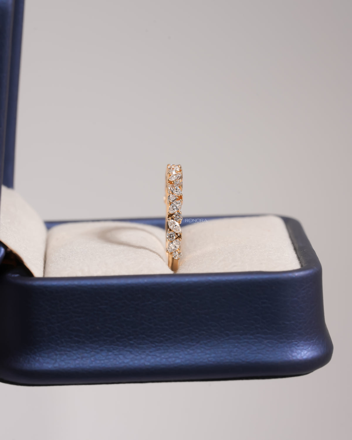 Side view of a marquise and round lab grown diamond wedding band in yellow gold standing in a blue ring box