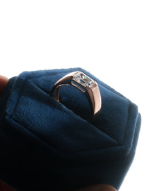 Rose gold men's east west emerald cut lab grown diamond ring with a flush bezel, angled in a blue velvet ring box