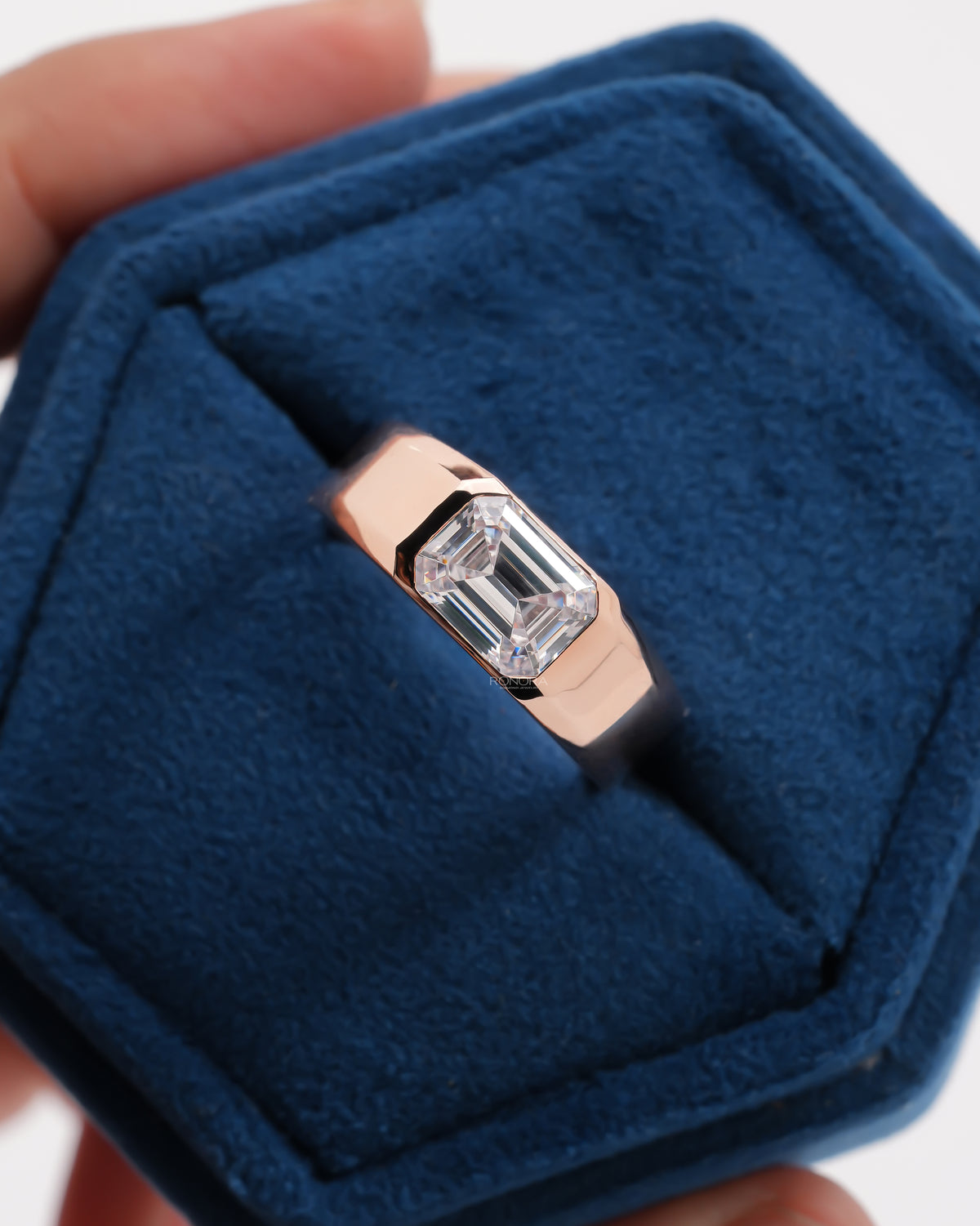 Close-up of a men's rose gold east west emerald cut lab grown diamond ring in a blue velvet ring box