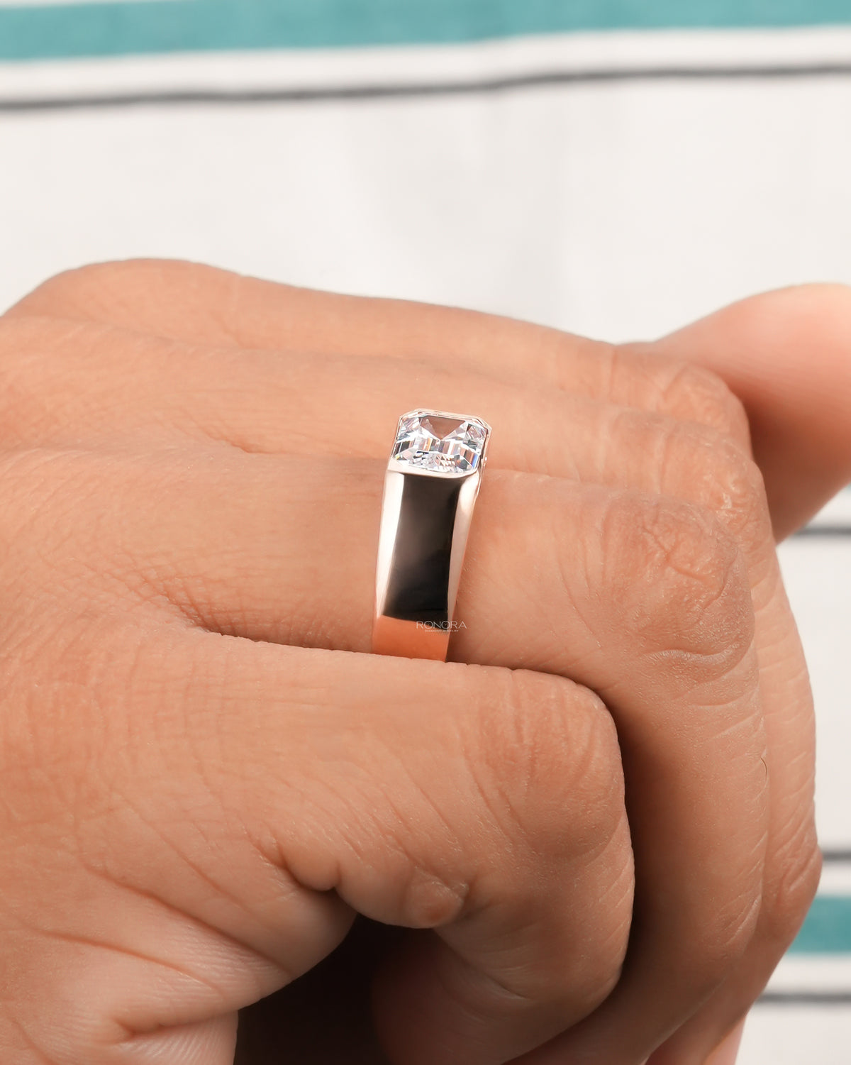 Side view of a men's rose gold emerald cut lab grown diamond ring worn on a finger, wide polished band
