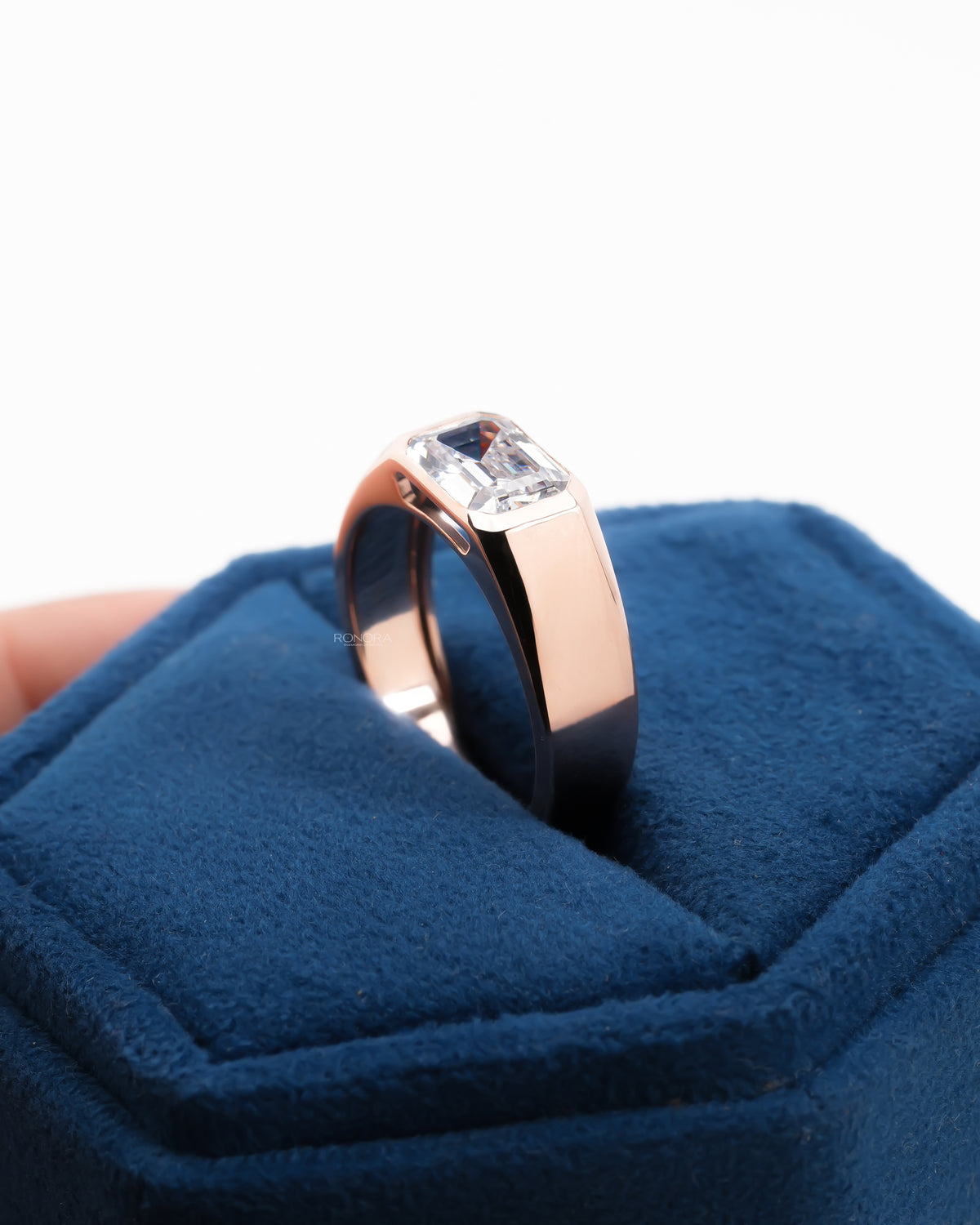Rose gold men's east west emerald cut lab grown diamond ring standing on a blue velvet ring holder