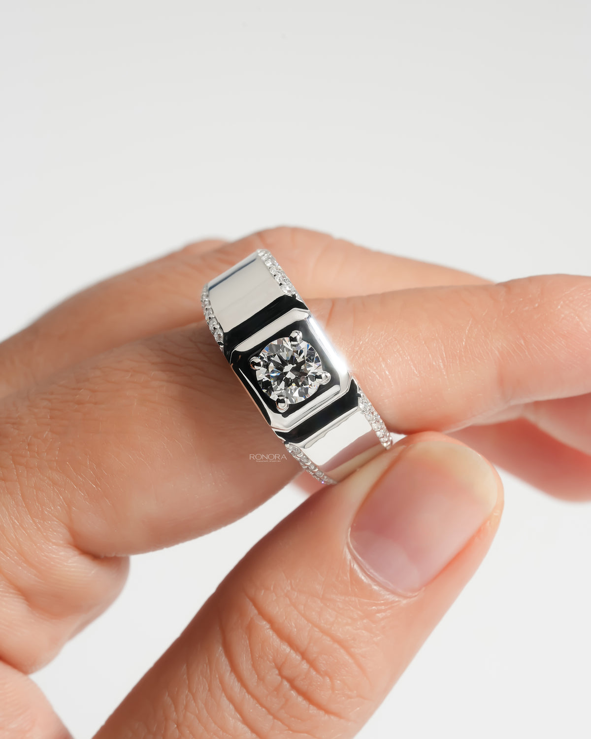Close-up of a men's round lab grown diamond ring on a finger, wide white gold band with pave set side diamonds